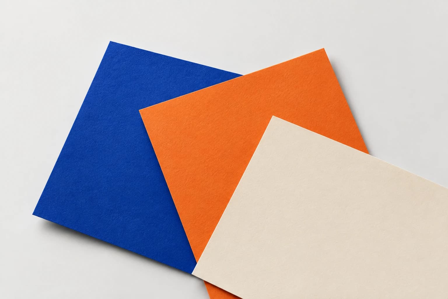 Overlapping blue, orange and cream paper swatches on a pale background.