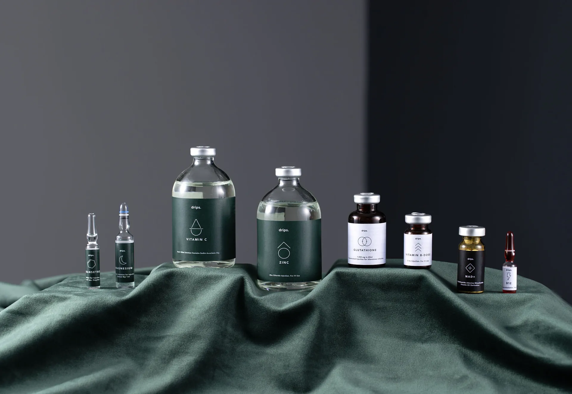 Drips vials and bottles of different sizes standing on dark green cloth.
