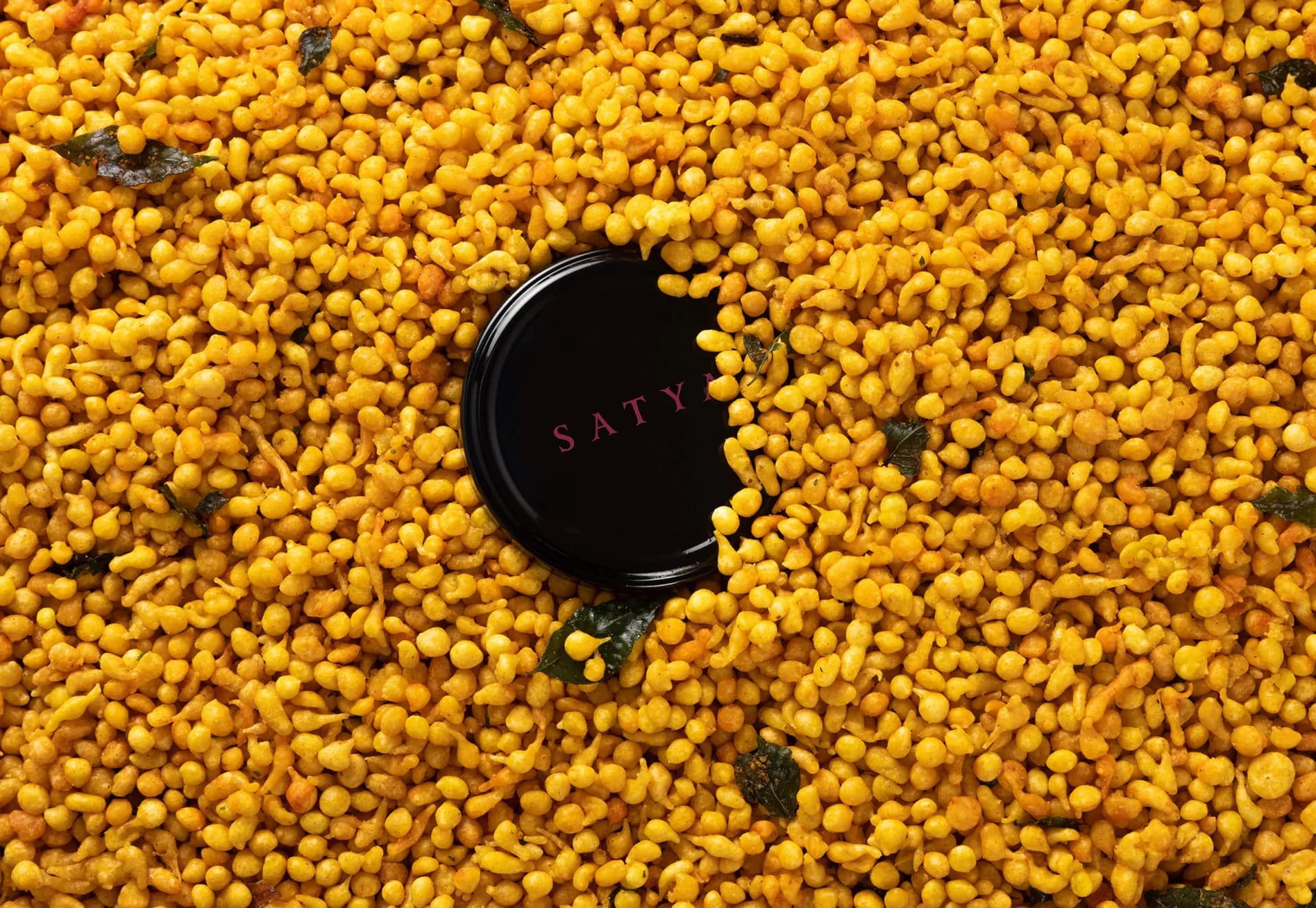 The black Satya lid in a spread of golden hummus drops.