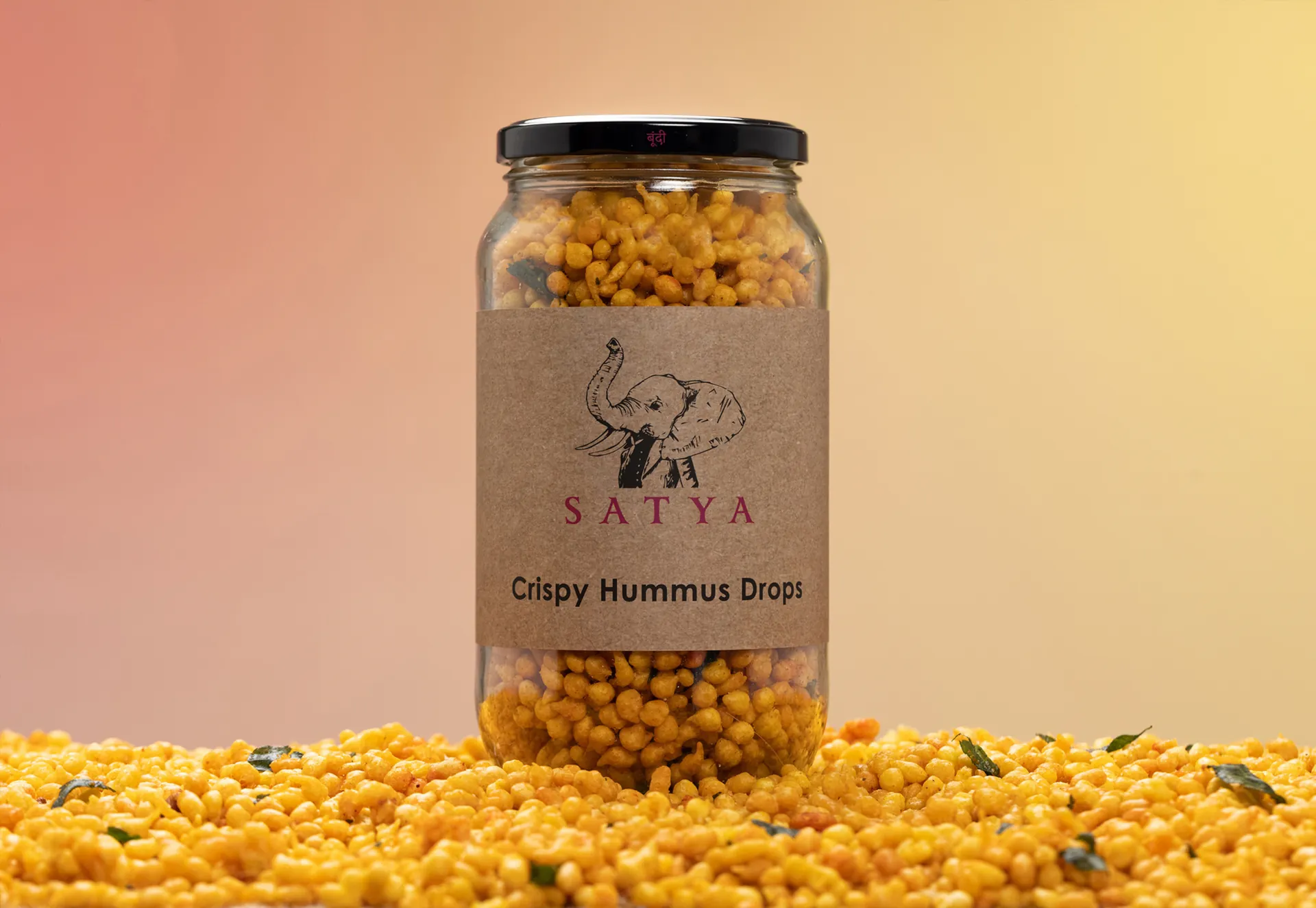 A Satya jar of Crispy Hummus Drops standing on a bed of hummus drops.