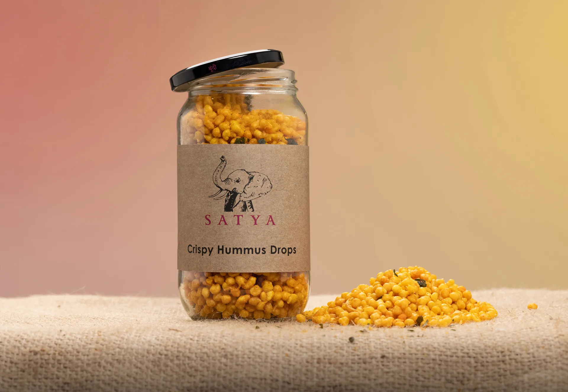 An open Satya jar beside a spill of hummus drops on hessian.