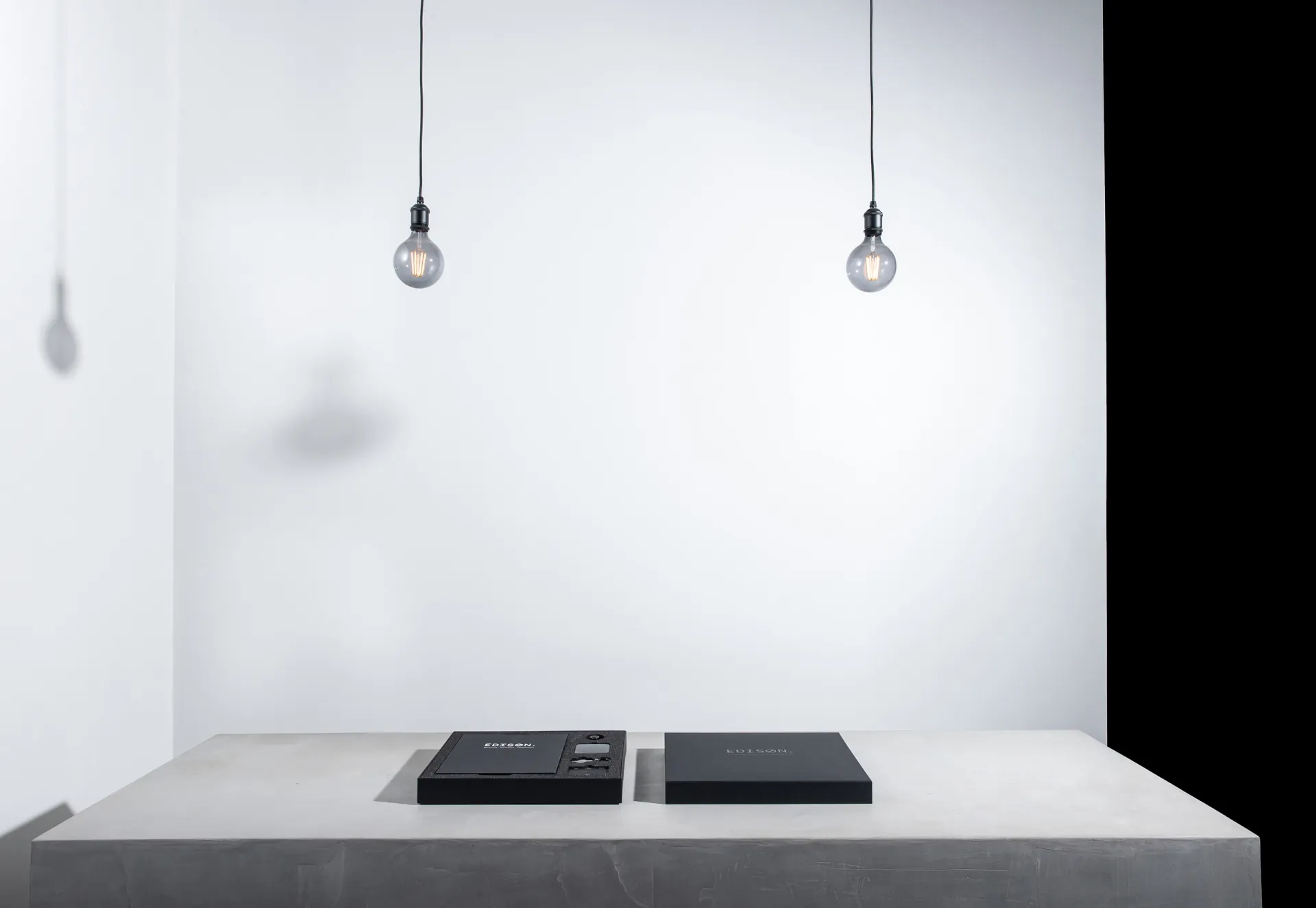 Two Edison kits on a long white plinth beneath two hanging bulbs.