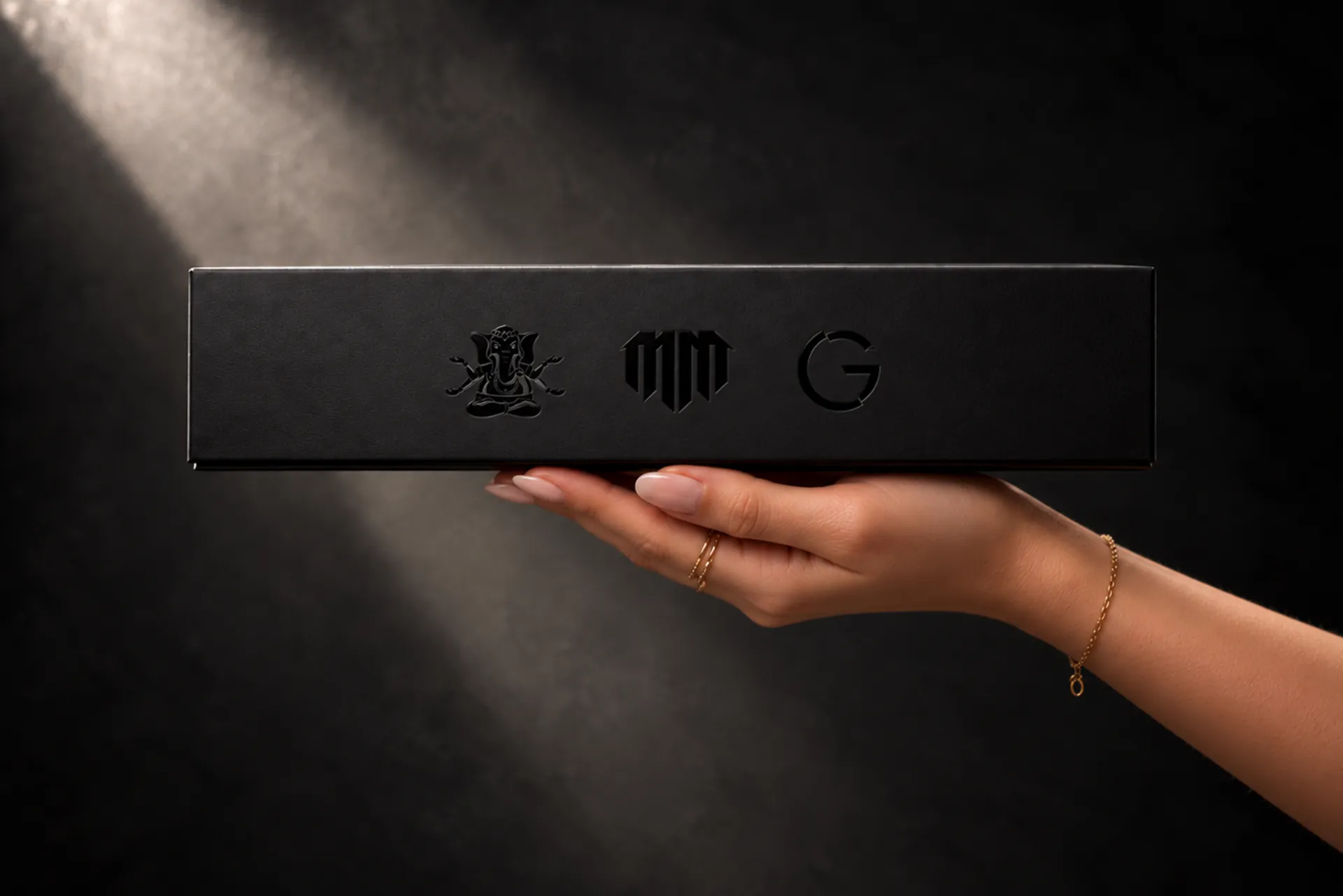 A black MadMac box held up on one hand in a shaft of light.