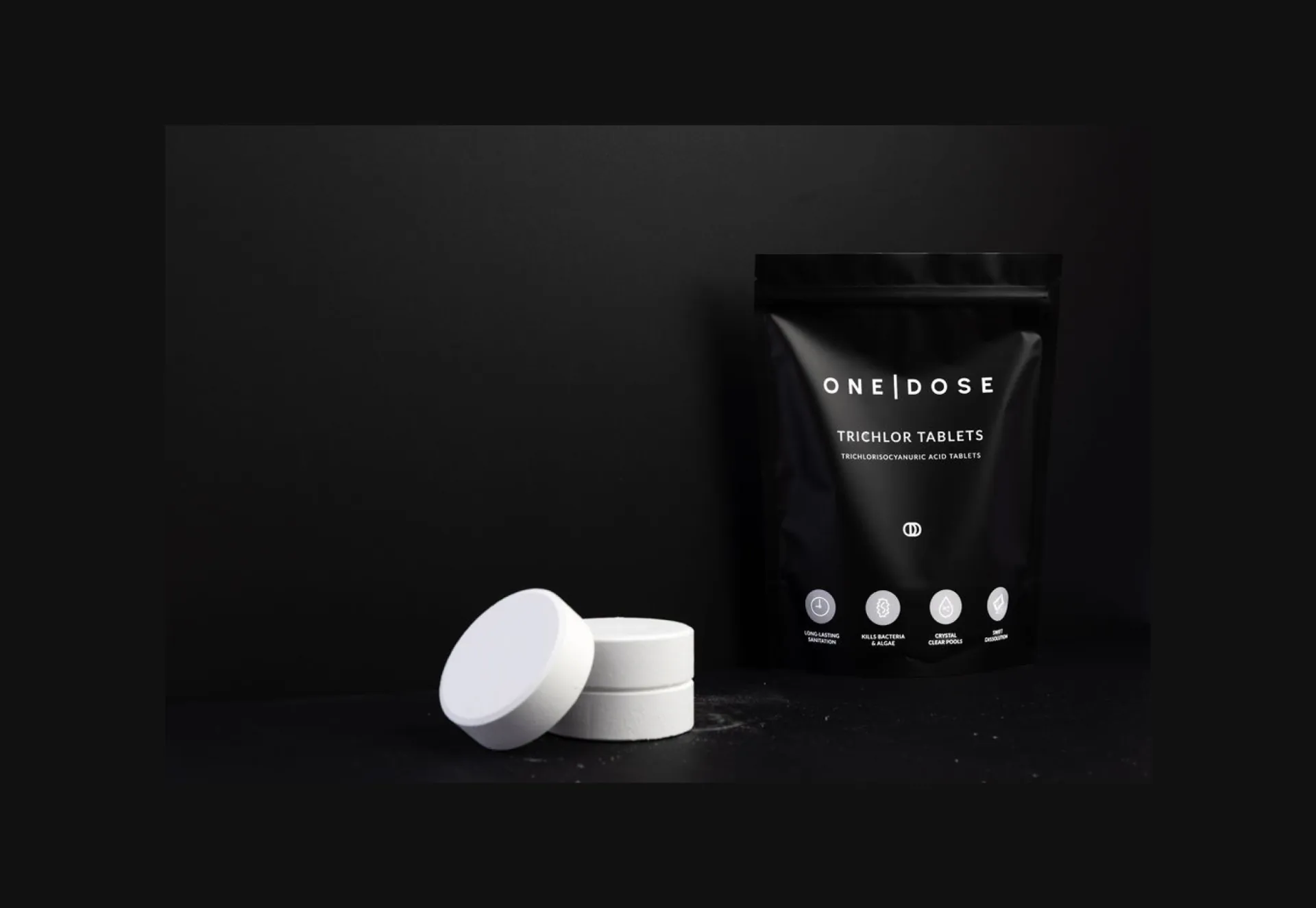 A black One Dose pouch of trichlor tablets, two white tablets stacked beside it.