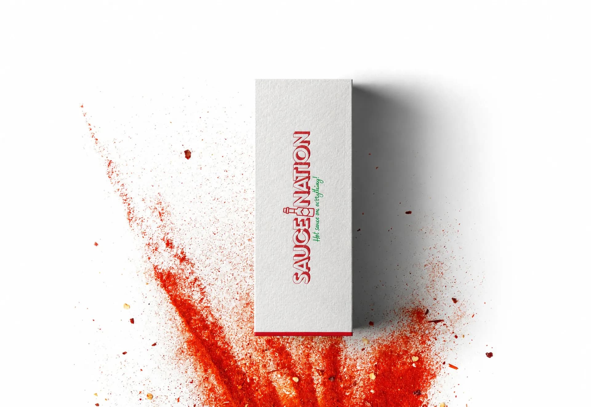 The white SauceNation presentation box standing in a burst of red chilli powder.