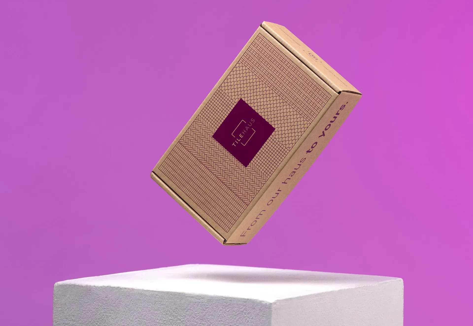 A kraft TileHaus box floating above a white plinth on a purple ground.